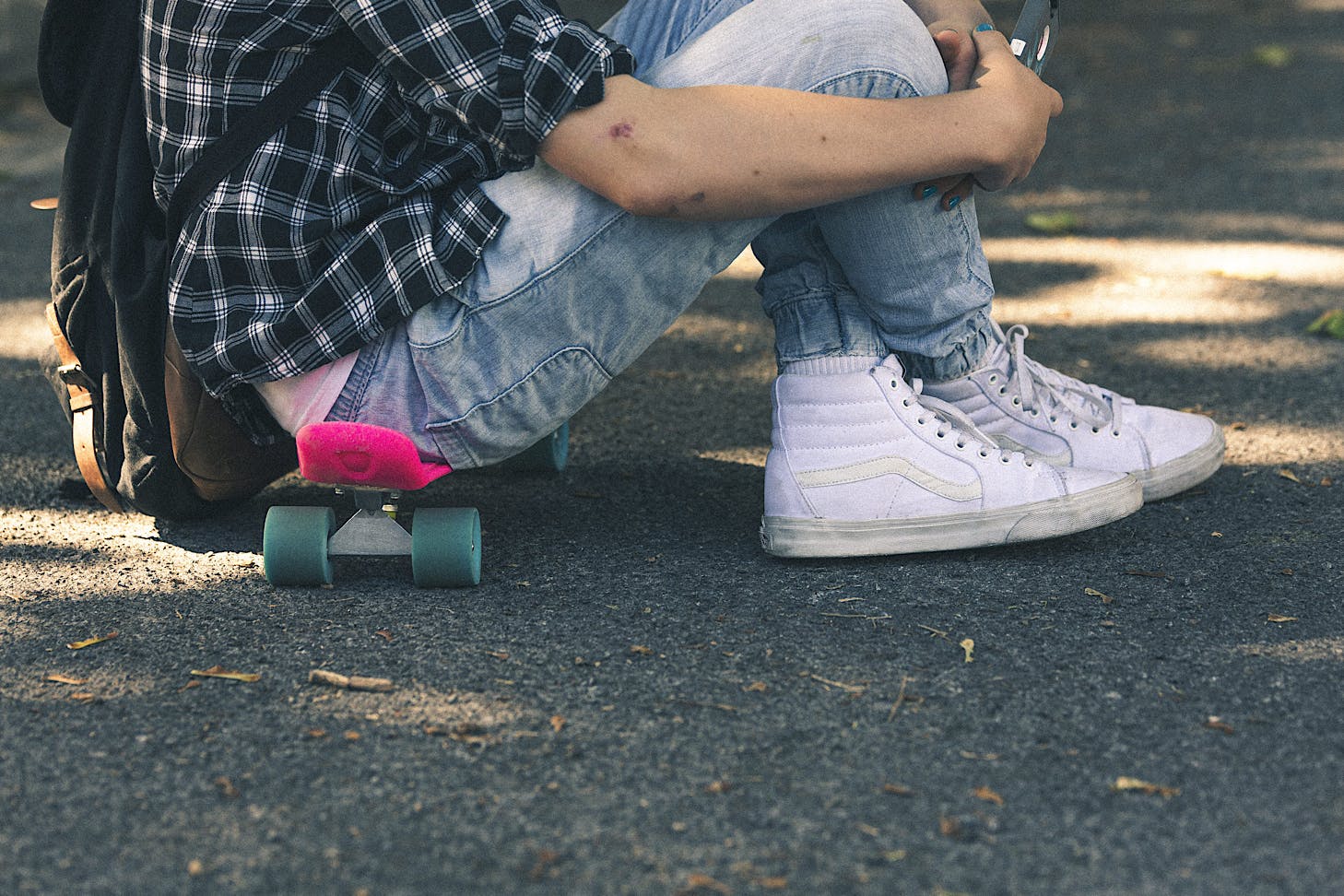 A kid sits on a pink skateboard and sports white kicks.